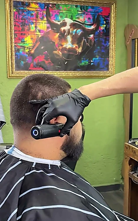 Barbero con guantes negros perfila con máquina la barba y el contorno de la oreja de un cliente.