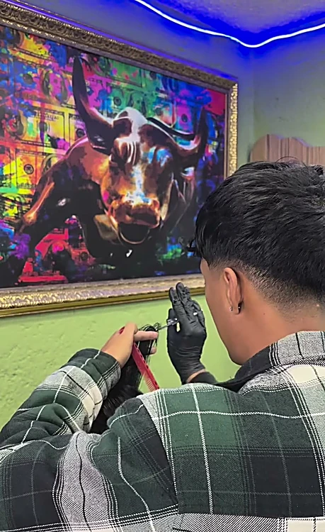 Barbero con camisa a cuadros corta con máquina frente al cuadro pop del toro.