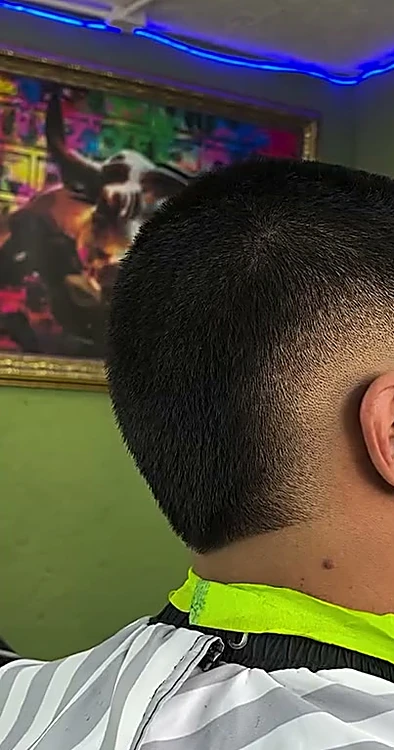 Fade bajo en la nuca de un cliente de espaldas, junto a un poste de barbero.